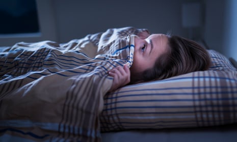 Woman looking scared under a blanket in bed