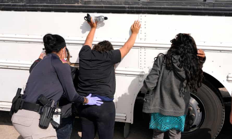 agent pats down woman with her hands on the side of a bus