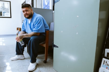 شخص يجلس على كرسي ويحمل زجاجة ماء ويميل قليلاً إلى الأمام لالتقاط صورة.