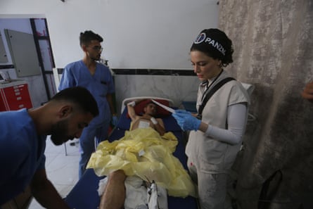 A wounded man lies on a hospital bed in Gaza surrounded by three medical staff