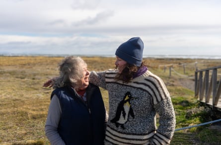 A young woman wearing a jumper with a penguin knitted into it puts her arm around an older woman as they both laugh