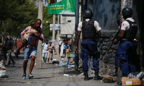 A parent, carrying his child after picking him up from school, runs past police carrying out an operation against gangs in Port-au-Prince, Haiti, earlier this month.