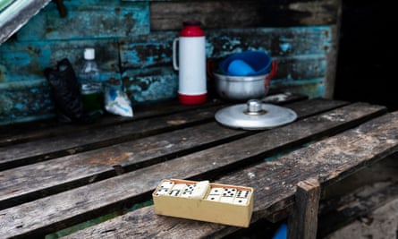 A domino set, some pots, and a thermos for coffee lie on a shaded wooden table.