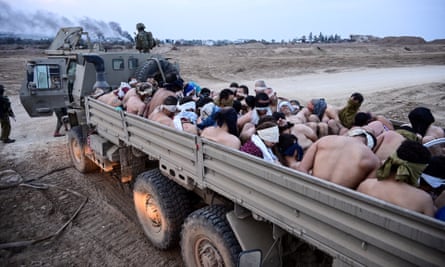 Israeli soldiers stand by a truck with shirtless Palestinian detainees.