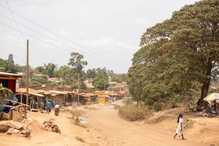 A woman crosses a dirt road that passes by a row of shacks