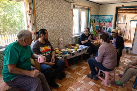 The group sit around a table with food and drink on it in a room