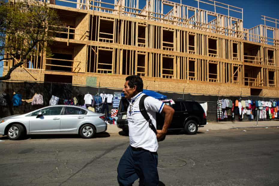 A man wearing a backpack walks down a street past a construction site.