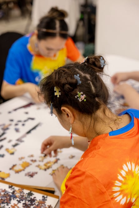 A woman in a tie-dye orange shirt wearing puzzle hair charms works on a puzzle