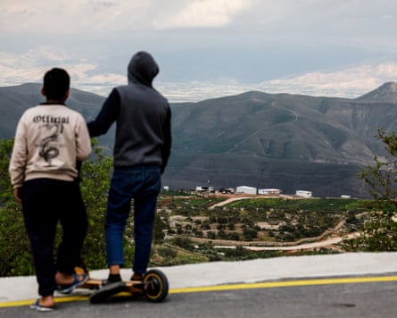 Two boys with their backs to the camera look out from a road to a settlement below Two boys with their backs to the camera look out from a road to a settlement below