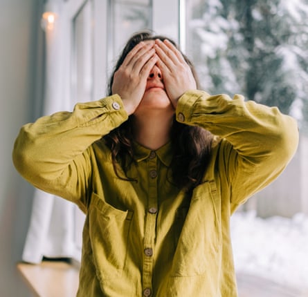 Woman covering her eyes with her hands by the window, expressing sadness and despair