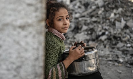 A Palestinian child holds an empty pot waiting to receive food distributed by volunteers.