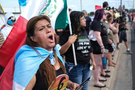 people at protest hold flags and signs while standing on side of road