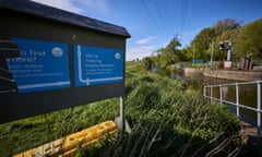 A blue Thames Water sign saying, 'We're making improvements', on a grassy bank next to water against blue sky