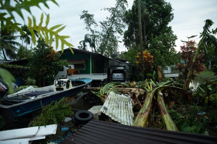 Debris and fallen trees lie on the ground next to a house