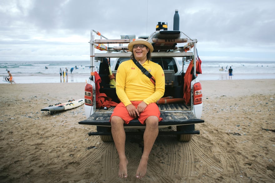 Lifeguard Aiden Coxhead sits smiling on the back of a lifeguard’s truck on the beach in Cornwall.