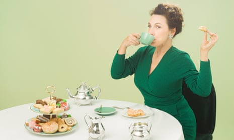 Grace Dent sitting at a table with a cake stand loaded with processed cakes and biscuits