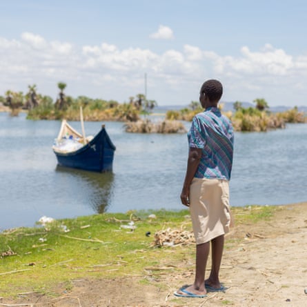 Woman stands on the shore of the lake looking out at a boat