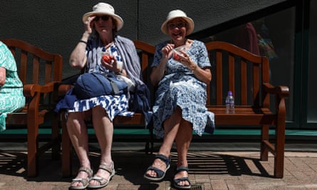 Two women enjoy strawberries on a bench at Wimbledon.