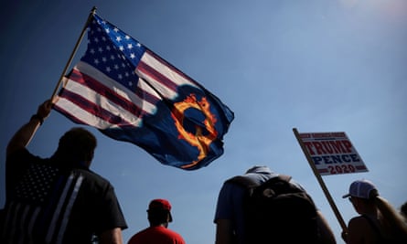 person holds american flag with Q on it, styled as fiery