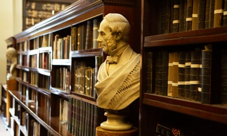 Kütüphanedeki kitap rafları arasında bir stand üzerinde bir büst.