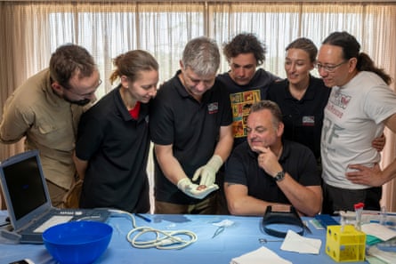 گروهی از مردم دور یک میز گرد می آیند تا جنین کرگدن را که در کف دست توماس هیلدبرانت، رئیس پروژه BioRescue نگهداری می شود، نگاه کنند.