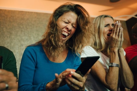 A woman texts her friends on her phone while watching a sporting match on the big screen late at night.