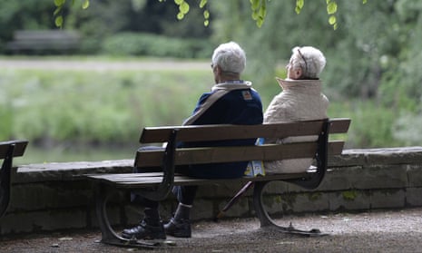 An elderly couple sits on a bench in a park 