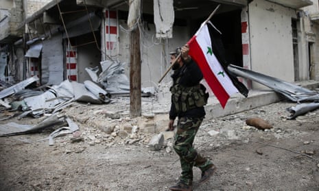 A Syrian soldier holds up the national flag as he patrols the east Aleppo neighbourhood of Tariq al-Bab.