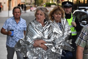 A police officer escorts members of the public, wrapped in foil blankets, towards The Shard in London