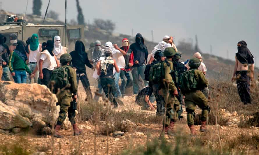 Israeli soldiers stand by as masked Israeli settlers throw stones at Palestinian protesters
