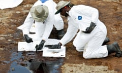 BP Plc contract workers are reflected in a pool of oil as they use absorbent pads to clean beach at Grand Isle State Park in Grand Isle, Louisiana, U.S., on Sunday, June 6, 2010