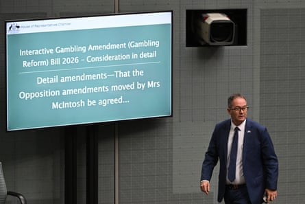 Andrew Wallace, wearing suit and tie, walks passed a screen with text outlining gambling reform bill amendments