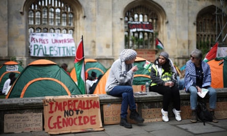 Three protesters sit on a wall next to the tents at the King’s College protest camp