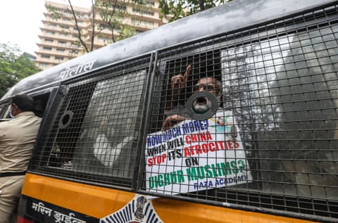 A bearded Indian man shouts through a van with a metal grill over the window. He holds a sign saying: ‘How much more? When will China stop its atrocities on Uyghur Muslims?’