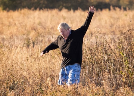 Boris Johnson running through tall grass in a black top and Bermuda shorts