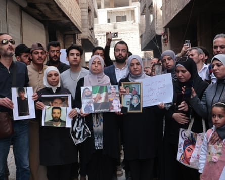 A large group of people hold up photos of relatives