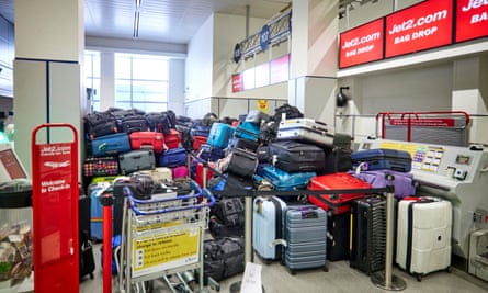 a large collection of bags and suitcases in many colours at the Jet2 departures hall at Manchester airport after a power cut: they are piled up at the check-in. No people are seen but there is an empty trolley in the foreground.