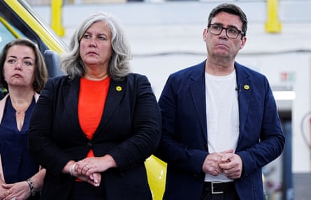Alexander stands alongside Burnham as they listen to a speech at a bus depot