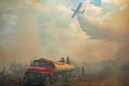 A plane flies above firefighters tackling a forest fire, 2020