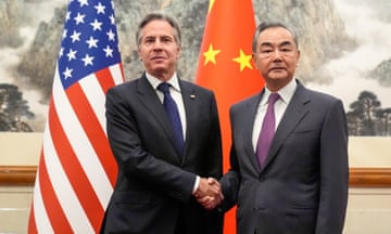 Antony Blinken shakes hands with  Wang Yi in front of their respective flags