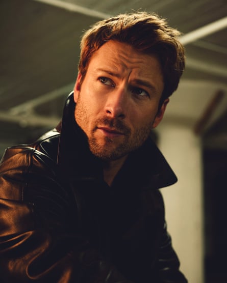 Portrait of Glen Powell looking to the right of the camera wearing a black leather jacket with the collar up