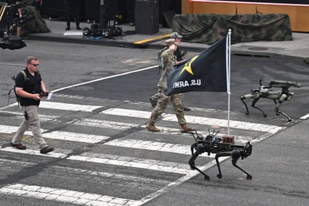 Three men walk along a road behind two mechanical dogs