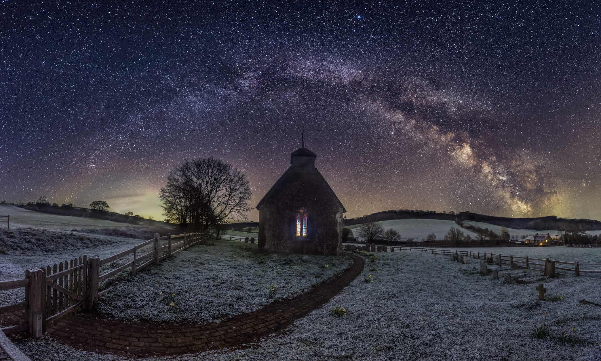 Snowy scene with stained-glass windowed church below the Milky Way galaxy