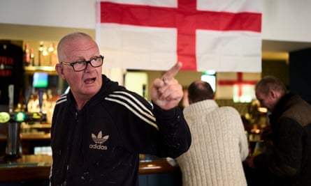 Mike Kneale points a finger while speaking in the pub, where St George’s flags hang from the ceiling