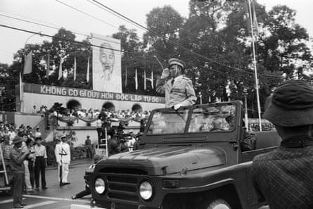 black and white photo of a man in a military uniform standing in car going through street