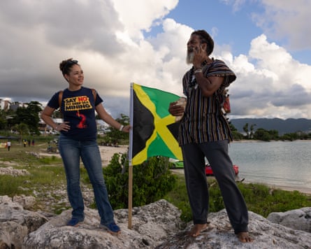 Theresa Rodriguez-Moodie holds a Jamaican flag beside a man speaking on a phone near the shore