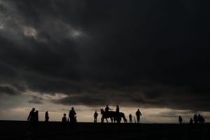People walk and ride horses in front of the Mediterranean Sea.