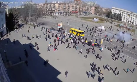 CCTV footage appears to show Russian troops (top, near building) firing stun grenades into a crowd of protesters, some with Ukrainian flags, amid the Russian invasion, along Ushakova Avenue in Kherson, Ukraine March 21, 2022