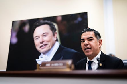 a man in a suit speaks from behind a dais next to a large photograph of a man