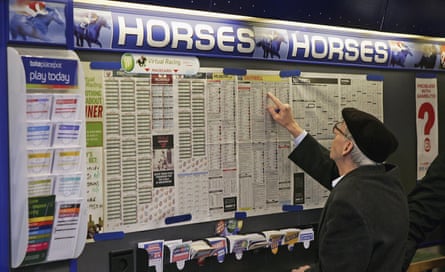 A man in a cap points at racing form sheets in a betting shop.